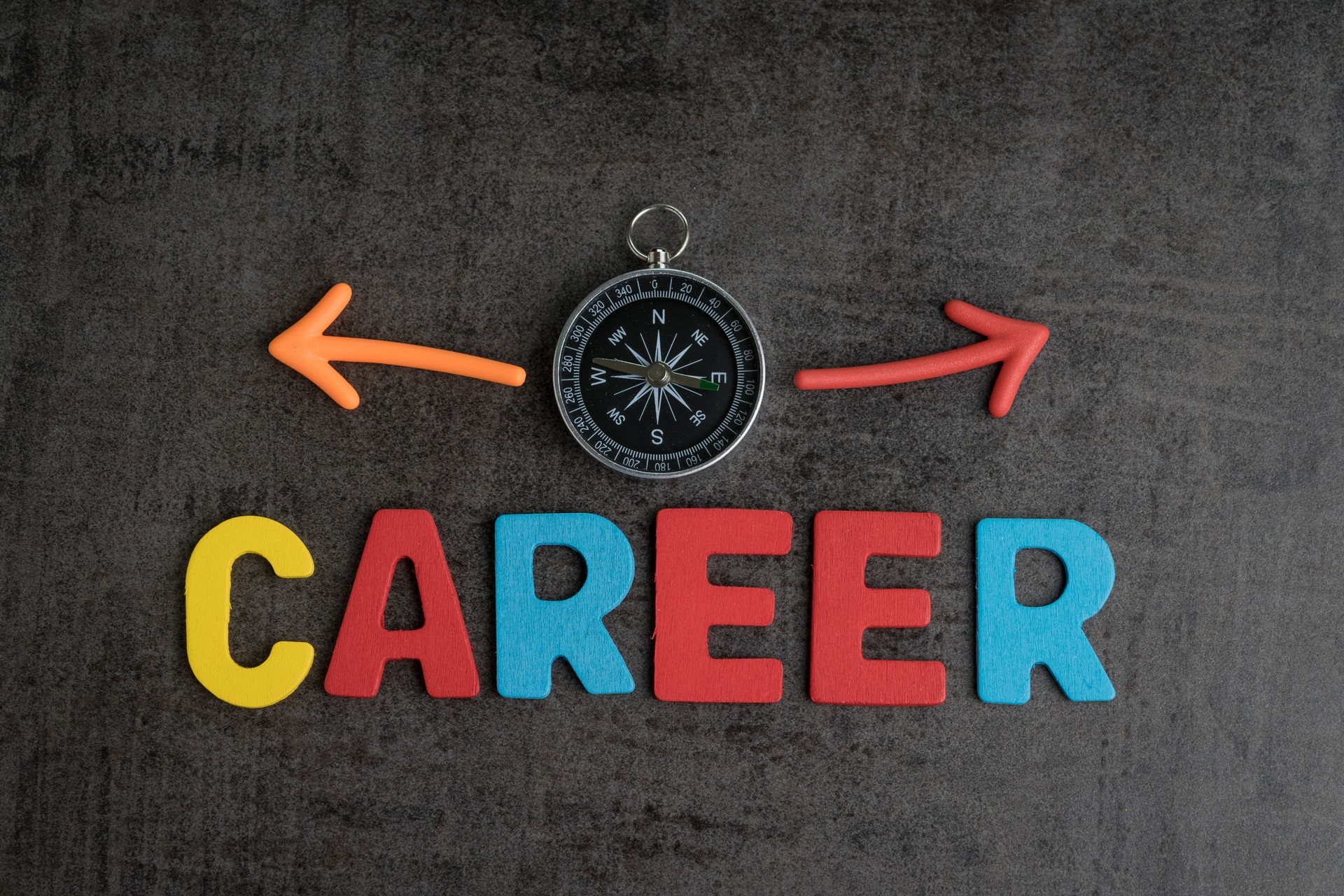 Company career path opportunities concept by colorful wooden alphabets as word CAREER and compass with magnet arrows pointing to left and right on dark black chalkboard cement wall